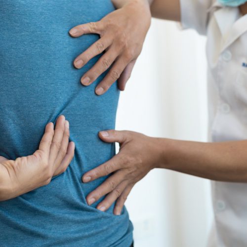 רופא בודק את גב המטופל היושב במרפאה ומצביע על אזור הכאב
